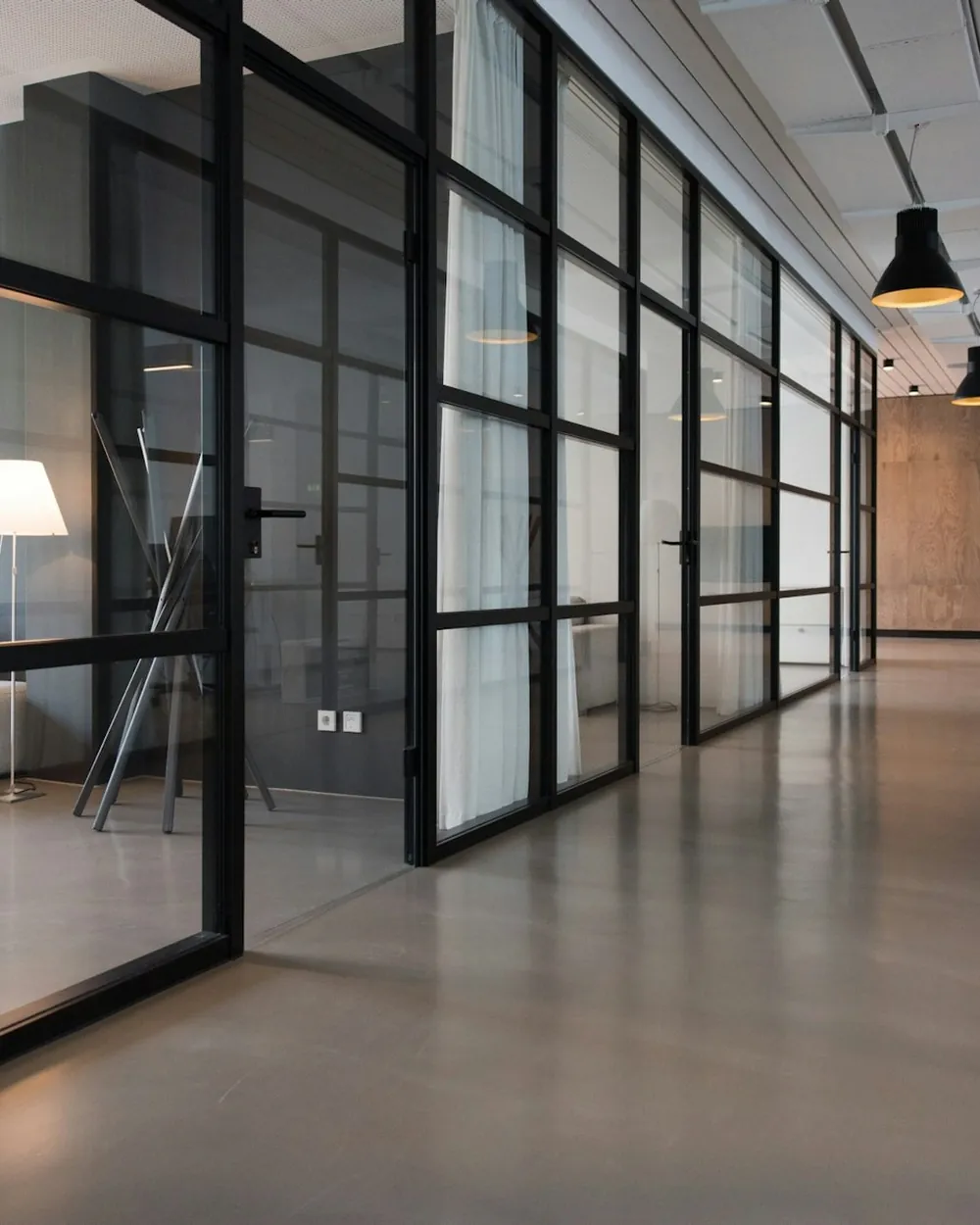 A minimal glass-walled office corridor with polished floors and warm lighting