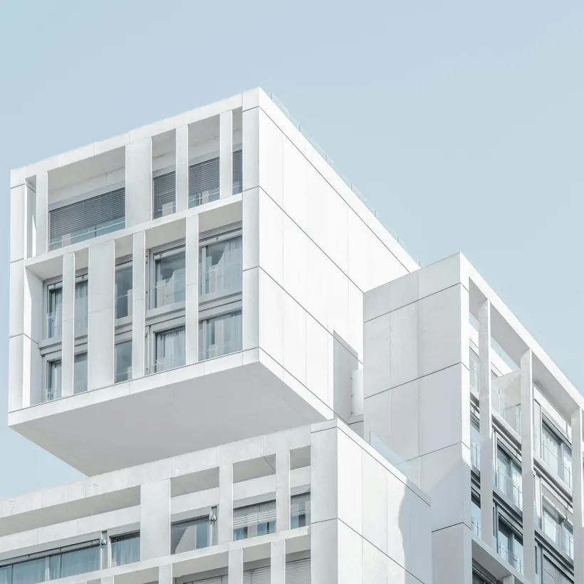 A white residential tower with stacked balconies against a clear sky